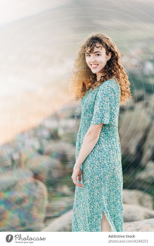 Lächelnde barfüßige Frau im Sommerkleid auf einem felsigen Hügel heiter Hochland Natur Sonnenkleid Zahnfarbenes Lächeln Barfuß sorgenfrei Felsen attraktiv