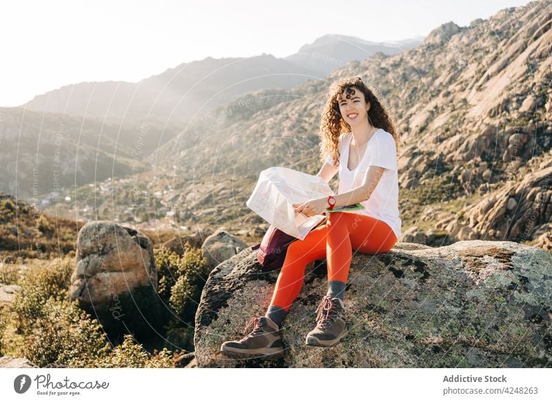 Fröhliche junge Frau sitzt auf einem Berghang und liest eine Karte Berge u. Gebirge Wanderer Landkarte Tal positiv lesen Glück Reisender Freude Urlaub