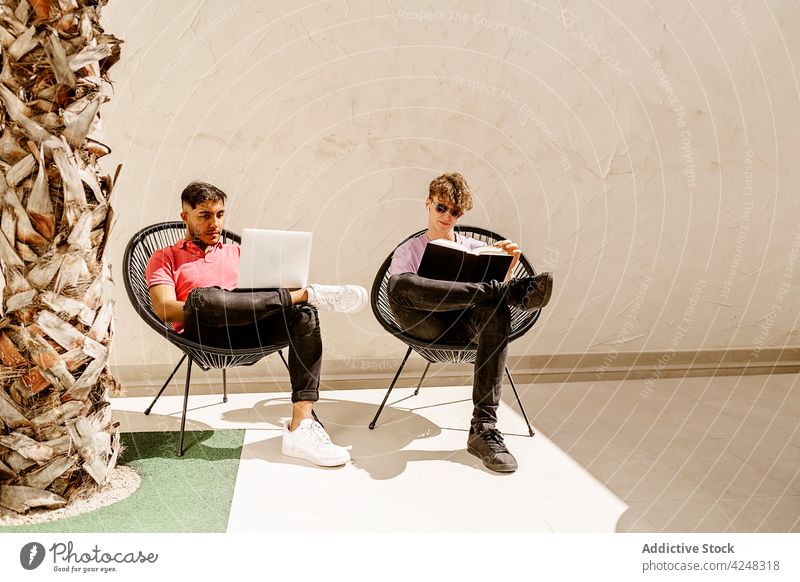 Trendige junge Leute entspannen sich auf der Terrasse mit Laptop und Buch Männer sich[Akk] entspannen lesen benutzend Zusammensein Freund Zeit verbringen