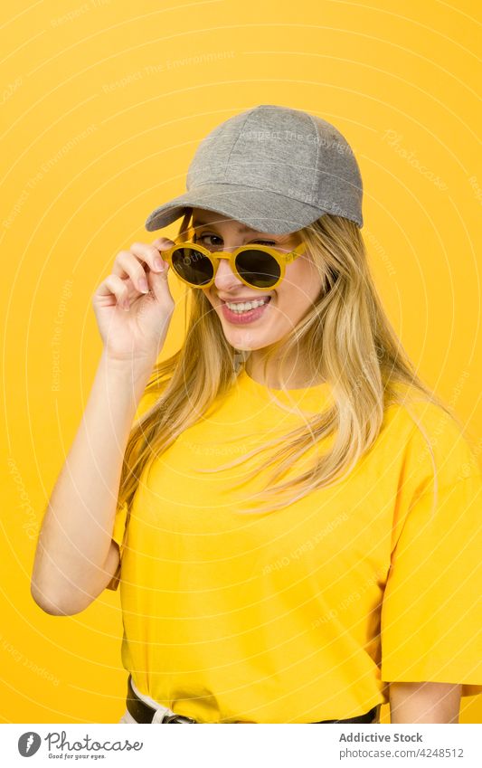 Frau mit Sonnenbrille in den Händen steht gegen gelbe Wand Stil lebhaft Hipster Streetstyle cool Vorschein Accessoire Pullover Verschlussdeckel jung lustig hell