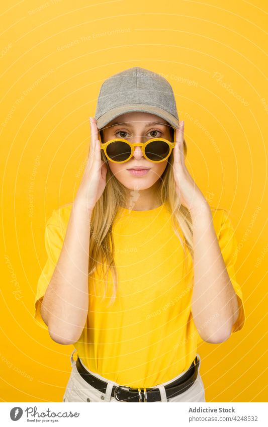 Frau mit Sonnenbrille in den Händen steht gegen gelbe Wand Stil lebhaft Hipster Streetstyle cool Vorschein Accessoire Pullover Verschlussdeckel jung lustig hell
