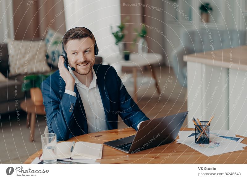Lächelnder gut aussehender junger Geschäftsmann mit Headset, der zu Hause online lernt Arbeit Mann heimwärts Büro reden Anruf Business Video Computer Anzug