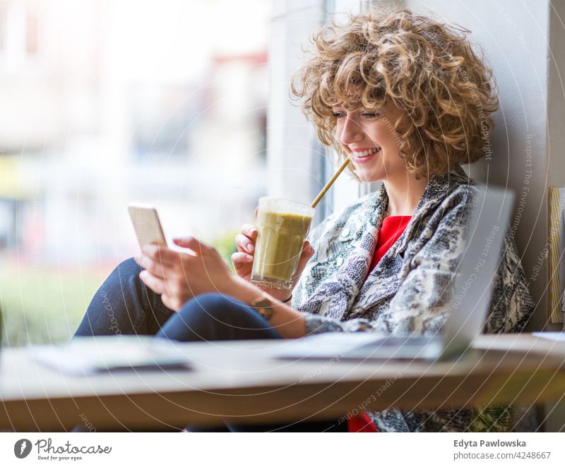 Junge Frau mit Mobiltelefon im Café genießend Lifestyle jung Erwachsener Menschen eine Person lässig Kaukasier positiv sorgenfrei Glück Lächeln attraktiv schön