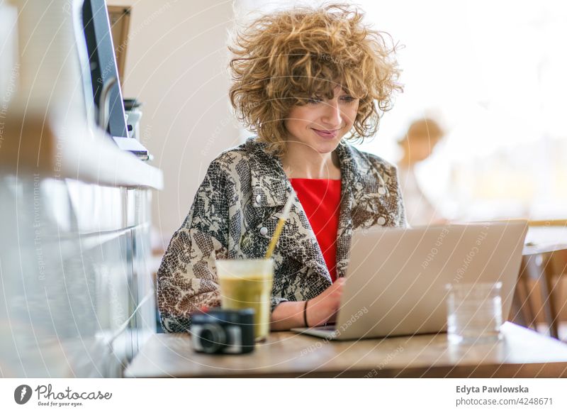 Junge Frau arbeitet an ihrem Laptop im Café genießend Lifestyle jung Erwachsener Menschen eine Person lässig Kaukasier positiv sorgenfrei Glück Lächeln