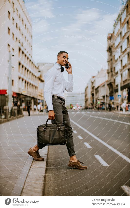 Junger afroamerikanischer Geschäftsmann, der ein Mobiltelefon benutzt, während er eine Straße überquert Amerikaner schwarz Gebäude Business Kabine Anruf Aufruf