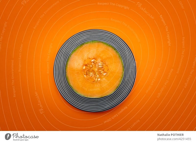 Halbierte Melone in der Draufsicht auf orangefarbenem Hintergrund Melonen Frucht Samen Hälfte geschnitten frisch Frische Teller geometrisch Design Flachlegung