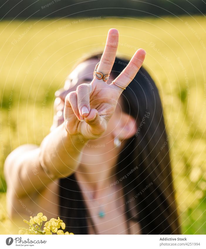Lächelnde Frau zeigt v-Zeichen auf blühendem Feld zwei Finger Zahnfarbenes Lächeln heiter gestikulieren Blütezeit Natur Glück Frieden Freude zeigen positiv jung