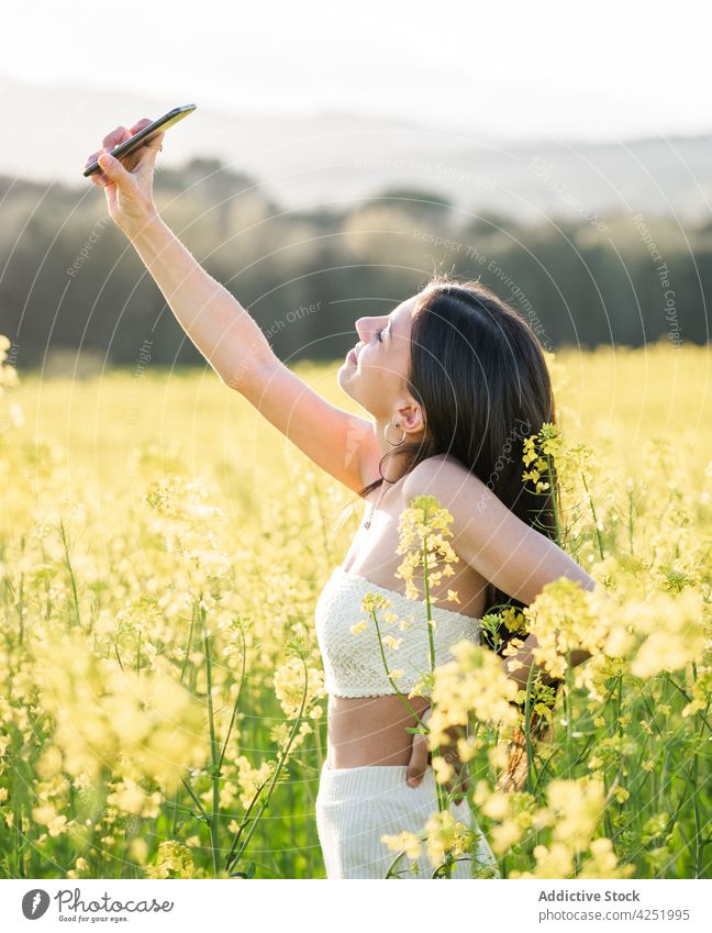 Glückliche Frau nimmt Selfie auf blühenden Feld Inhalt Lächeln Smartphone fotografieren Blütezeit Landschaft Wiese Blume Selbstportrait Fotografie Moment Mobile
