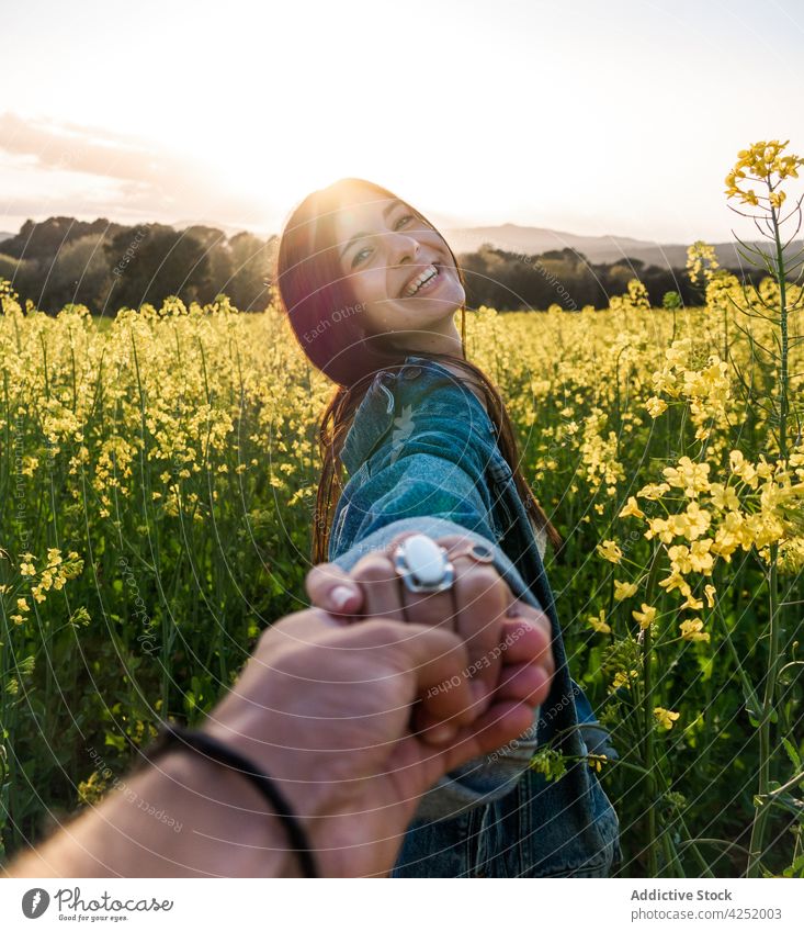 Fröhliche Frau hält die Hand ihres Freundes und steht auf einem blühenden Feld Paar mir folgen freudig Blütezeit Händchenhalten Zahnfarbenes Lächeln heiter