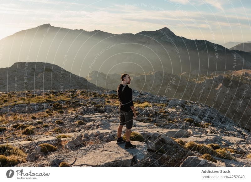 Unbekannter Mann auf rauem Berggipfel ruhend Wanderer Berge u. Gebirge Hochland Sonnenuntergang bewundern Natur Reisender Trekking stehen nachdenklich Felsen