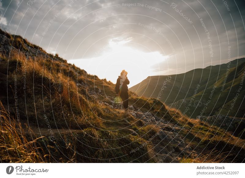 Wandernde Frau am Hang eines Berges bei Sonnenuntergang Wanderung bergab Spaziergang Tal Berge u. Gebirge Rucksack Hochland erkunden Hügel Reisender Gras