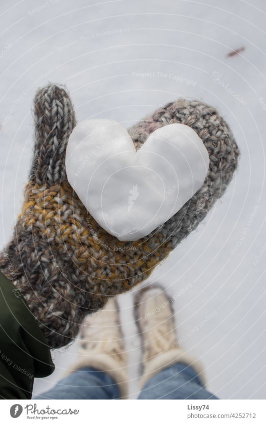Ein aus Schnee geformtes Herz , gehalten von einer in Handschuhen eingepackten Hand Schneeherz Winter Fäustlinge Strick Wollhandschuhe bunt hygge Natur