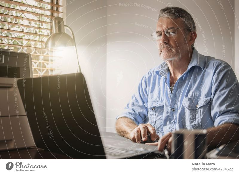 Ein älterer Mann sitzt an einem Schreibtisch vor einem Laptop-Computer Business Technik & Technologie Krypto Handel Finanzen Person Blockkette Tabelle kaufen