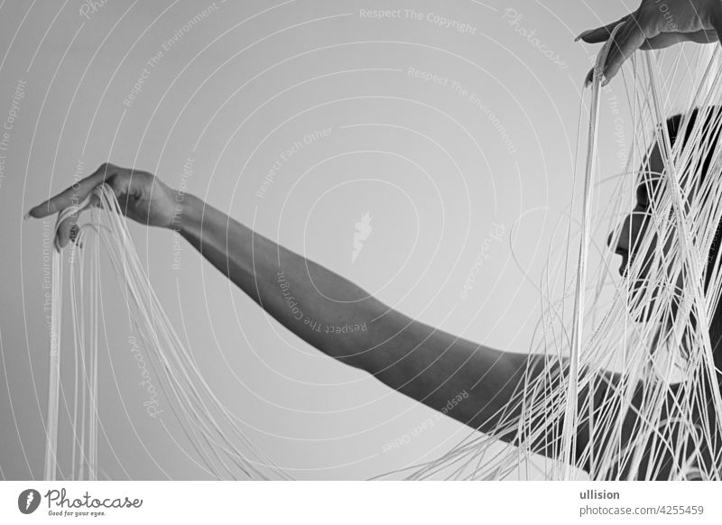 schwarz-weiß Abbildung des Profils einer jungen attraktiven Frau mit unbedeckten Schultern, die mit ihren Händen dekorativ die weißen Fäden eines Fadenvorhangs zieht, Kopierraum