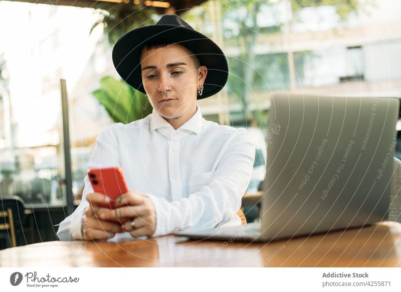 Tomboy surft auf dem Handy, während er am Laptop arbeitet Frau Wildfang benutzend Smartphone freiberuflich Arbeit Transgender agender queer Browsen transsexuell