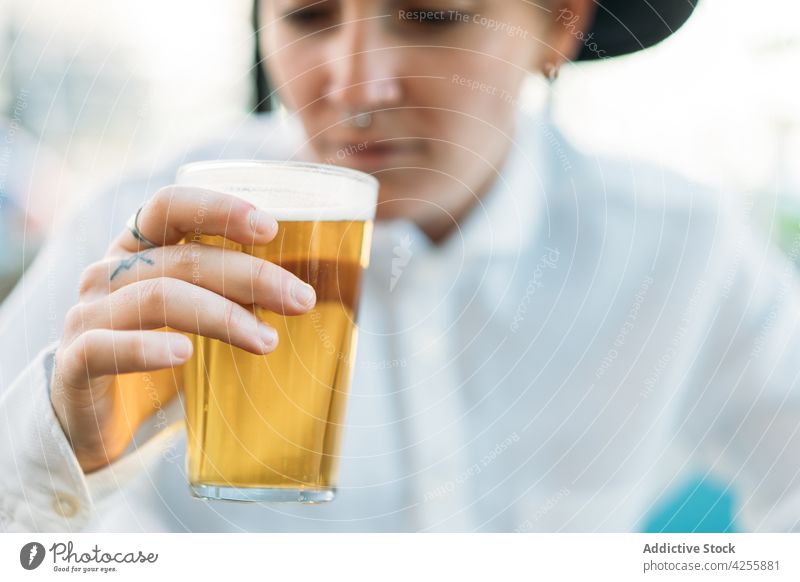 Lächelnde queere Frau trinkt Bier am Tisch Wildfang Schnaps Geschmack Alkohol Glas brauen Transgender agender Identität schäumen Getränk Becher Erfrischung