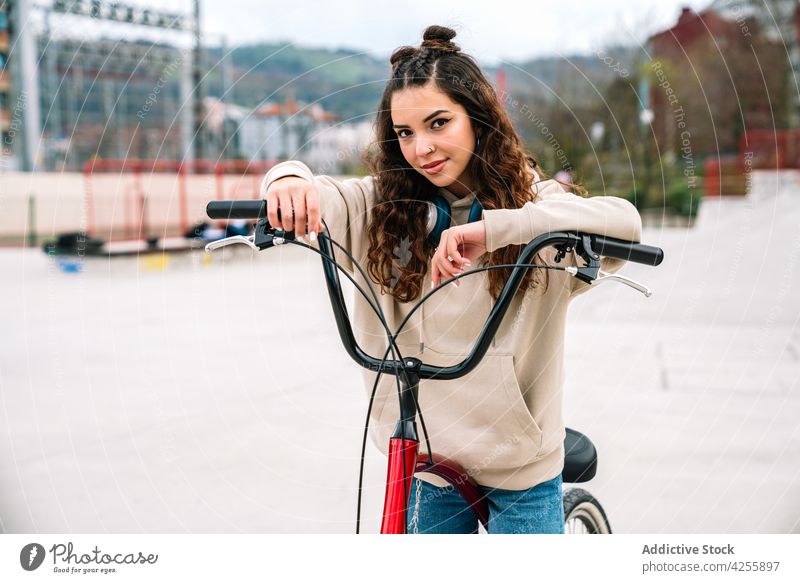 Positive Frau auf dem Fahrrad in einem Stadtpark positiv Lächeln heiter Mitfahrgelegenheit Großstadt Aktivität urban Glück Kapuzenpulli Jeanshose Hobby aktiv