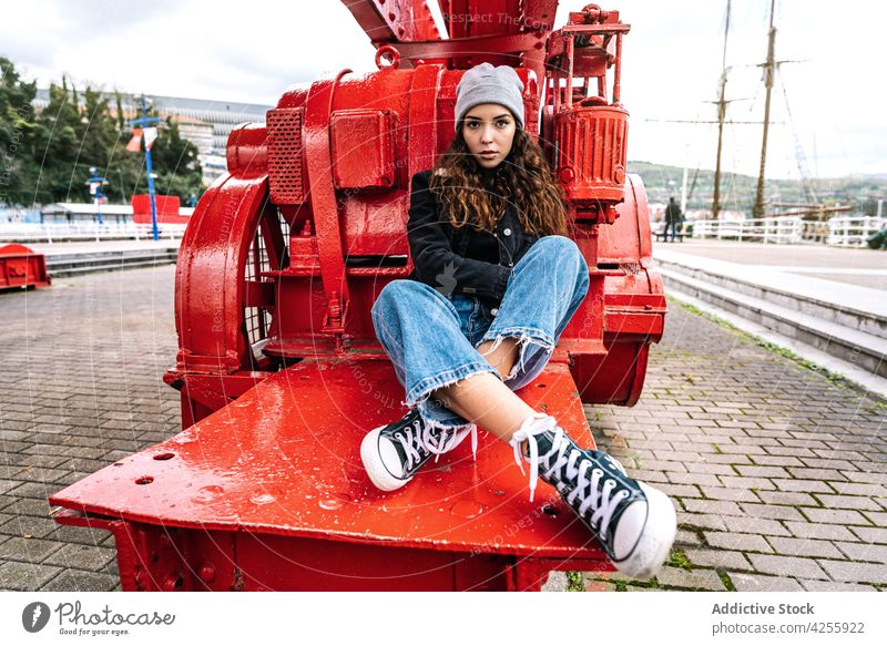 Frau in Jeans und warmer Kleidung auf Metallkonstruktion ruhend Jeanshose warme Kleidung selbstbewusst Konstruktion Oberbekleidung urban nachdenken cool jung