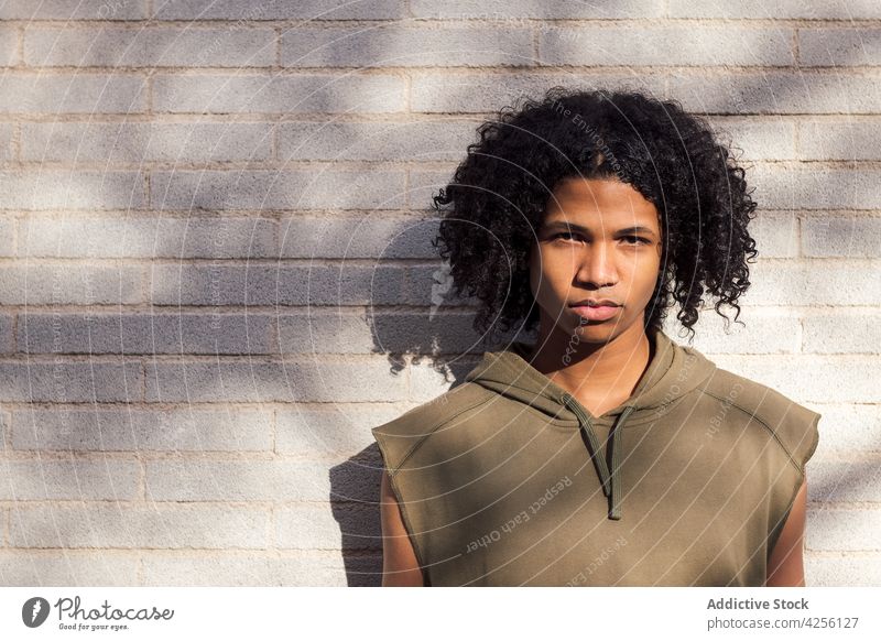 Ernster, schwarzer, lockiger Mann im Sonnenlicht stehend Teenager tausendjährig cool Youngster sorgenfrei ernst Afro-Look Vorschein Blick männlich