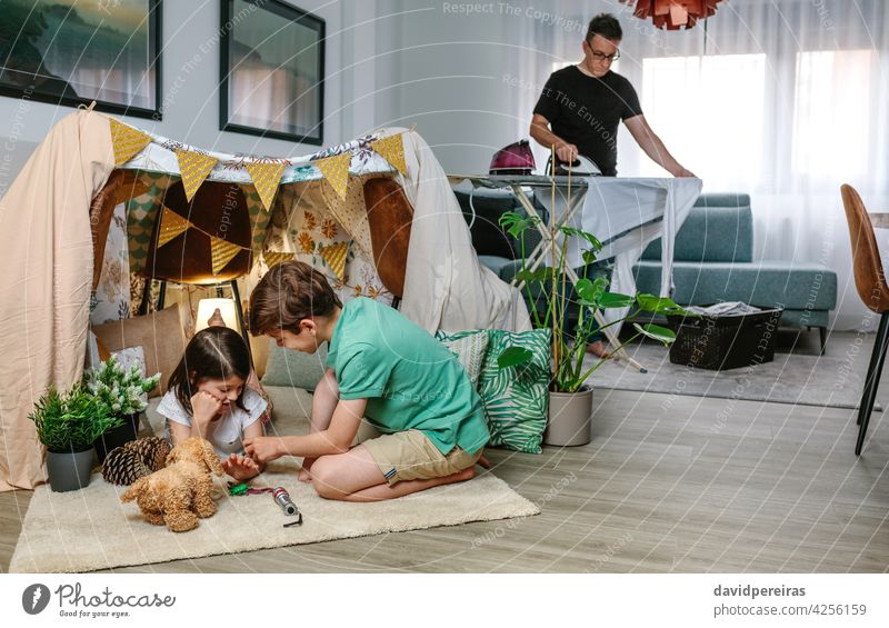 Vater bügelt, während ihre Kinder zu Hause Camping spielen bügelnd Kleidung Zelt heimwärts Familienschlichtung beschäftigt Zusammensein Wohnzimmer Hausmann