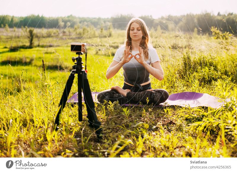 Das Mädchen praktiziert Yoga in der Natur und nimmt eine Videostunde über Yoga auf. Yoga online, Ausbildung online Fotokamera Lektion Pose Gesundheit Fitness