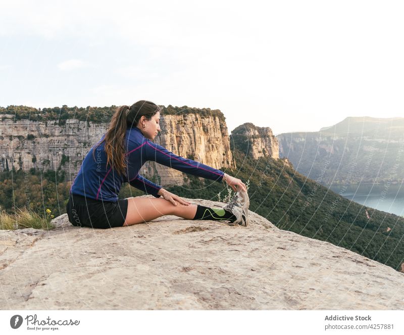 Junge ethnische Frau ruht sich nach einem Training in den Bergen auf einer Felsklippe aus Dehnung Berge u. Gebirge Klippe Athlet Natur Konzentration Wellness