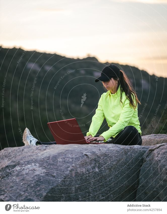 Weibliche Fernarbeiterin mit Laptop auf einer felsigen Klippe über einem Fluss bei Sonnenuntergang Frau Arbeit Berge u. Gebirge freiberuflich Browsen Natur