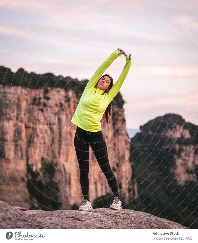 Junge hispanische Sportlerin, die ihren Körper beim Training in felsigen Bergen dehnt Frau Dehnung Berge u. Gebirge Übung Aufwärmen Wellness Gesundheit