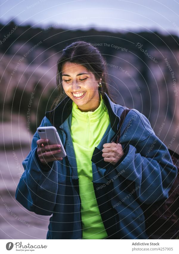 Fröhliche junge ethnische Frau lächelt und benutzt ihr Smartphone auf einer felsigen Klippe Nachricht Lächeln Schlucht Reisender Trekking Berge u. Gebirge