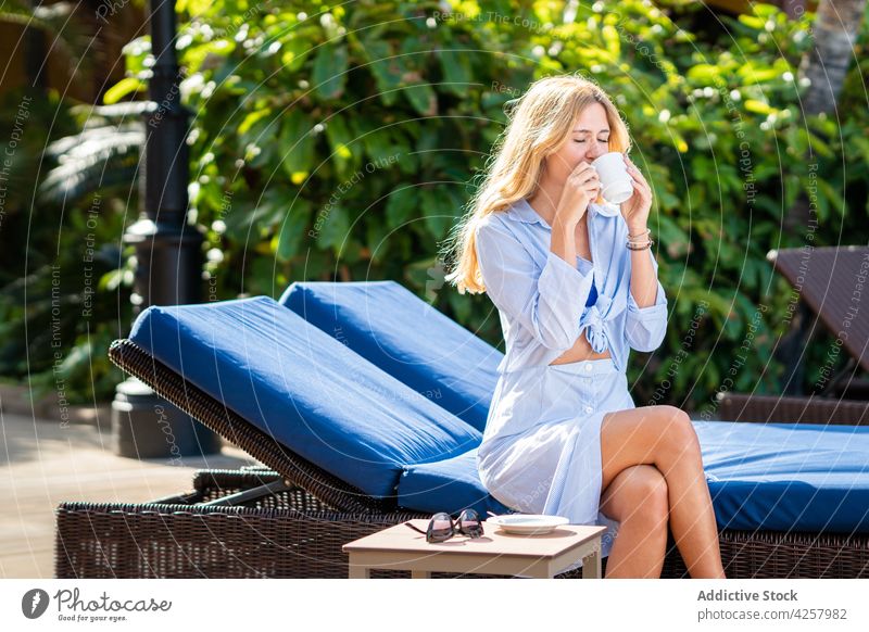 Lächelnde Frau, die ein heißes Getränk genießt und auf einem Liegestuhl sitzt trinken Zahnfarbenes Lächeln Glück Kälte sorgenfrei Erholung Resort Sonnenbank