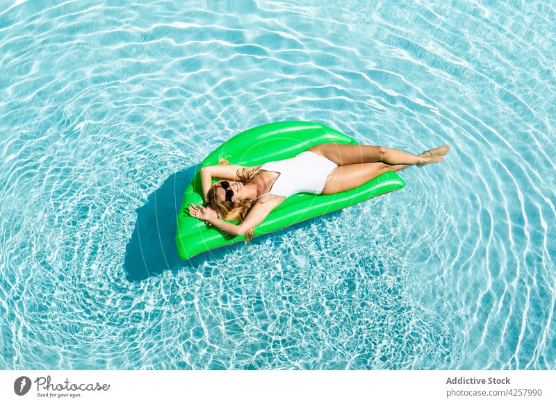 Attraktive fröhliche Frau schwimmt auf Luftmatratze im Pool Kälte Badebekleidung Zahnfarbenes Lächeln Sonnenbad Bräune Paradies Resort aufblasbar schwimmen