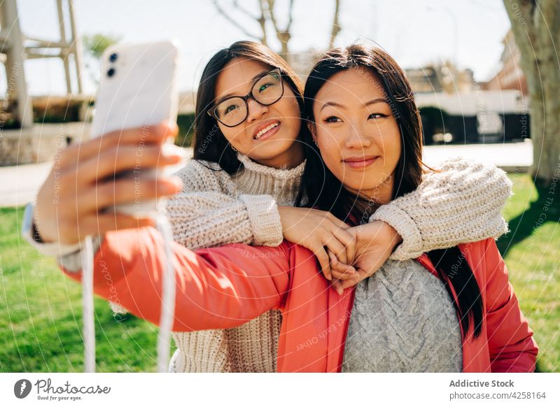 Erfreute junge asiatische Frauen zeigen das Friedenszeichen, während sie ein Selfie im Park machen Lächeln Smartphone Freund v-Zeichen Freude Zeit verbringen