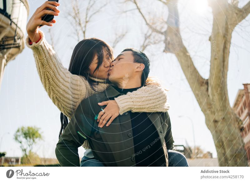 Liebevolles junges asiatisches Paar macht Selfie beim Kuscheln und Küssen im Park Kuss kuscheln Termin & Datum Zuneigung Smartphone Zusammensein Umarmung