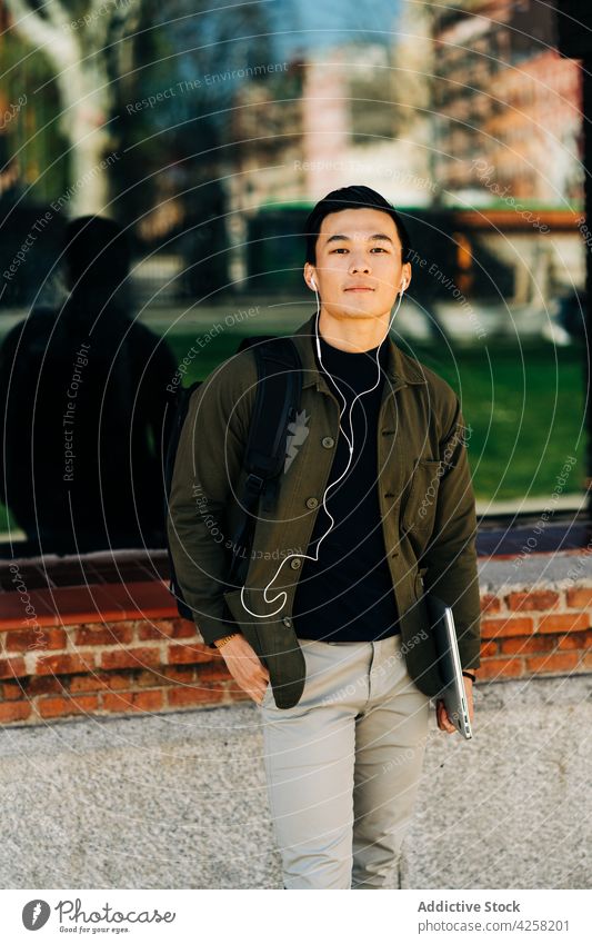 Glücklicher junger asiatischer Mann, der beim Gehen auf der Straße Musik über Kopfhörer hört zuhören Lächeln Großstadt Stil Gesang positiv Optimist Gebäude
