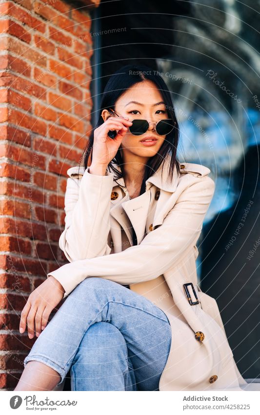 Stilvolle junge ethnische weibliche Millennial Anpassung Sonnenbrille auf der Straße Frau selbstsicher selbstbewusst trendy ruhen Großstadt ausrichten ernst