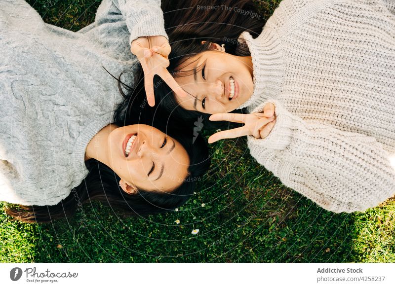 Junge asiatische Damen zeigen V-Zeichen und lächelnd, während sie auf Gras im Sonnenlicht liegen Frauen Lächeln Lügen Rasen bester Freund heiter v-Zeichen
