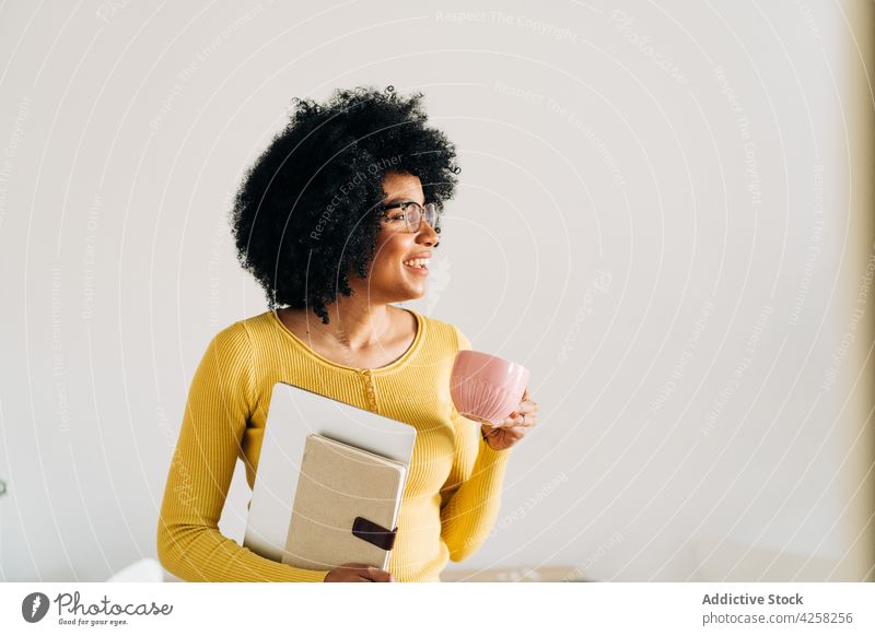 Schwarze Frau mit Brille, Tasse und Notebook mit Laptop klug heiter Lächeln positiv Becher Kaffee Heißgetränk gelb Pullover modern schwarz sich[Akk] entspannen