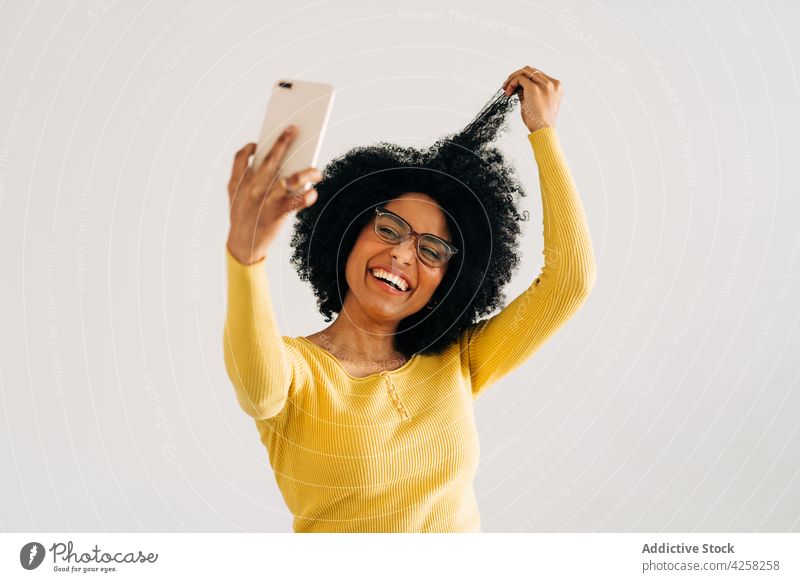 Glückliche schwarze Frau mit Brille lächelt und macht ein Selfie Lächeln positiv Smartphone heiter Mobile Telefon sorgenfrei gelb Pullover Selbstportrait Freude