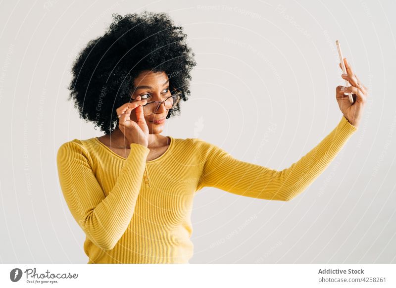 Glückliche schwarze Frau mit Brille lächelt und macht ein Selfie Lächeln positiv Smartphone Mobile Telefon sorgenfrei gelb Pullover Selbstportrait Freude