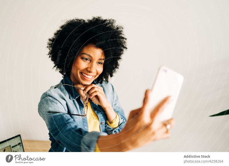 Glückliche schwarze Frau mit Brille lächelt und macht ein Selfie Lächeln positiv Smartphone Mobile Telefon sorgenfrei gelb Pullover Selbstportrait Freude