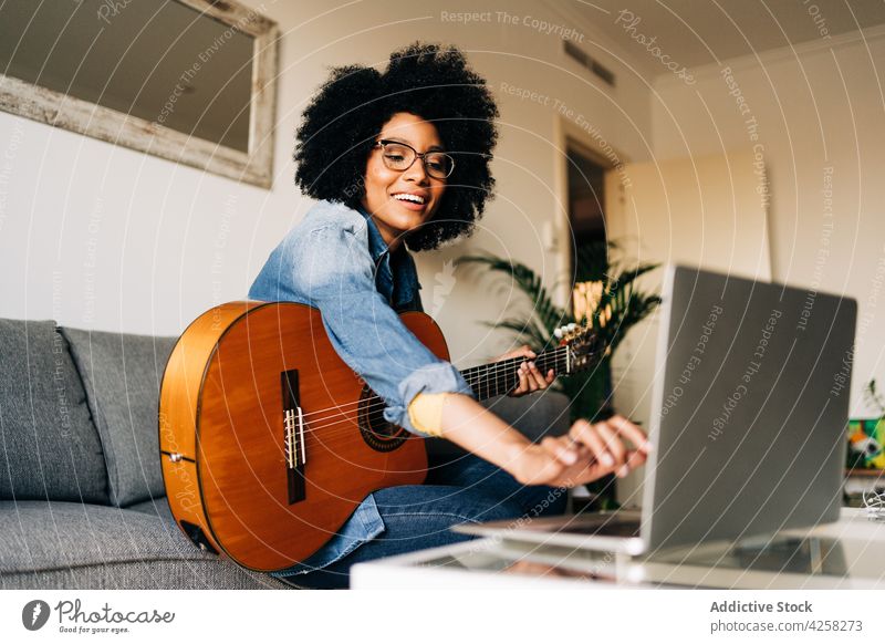 Positive schwarze Frau spielt Gitarre zu Hause Musiker Laptop singen Aufzeichnen spielen Podcast Hobby Gesang vlog Lächeln online Gitarrenspieler heimwärts