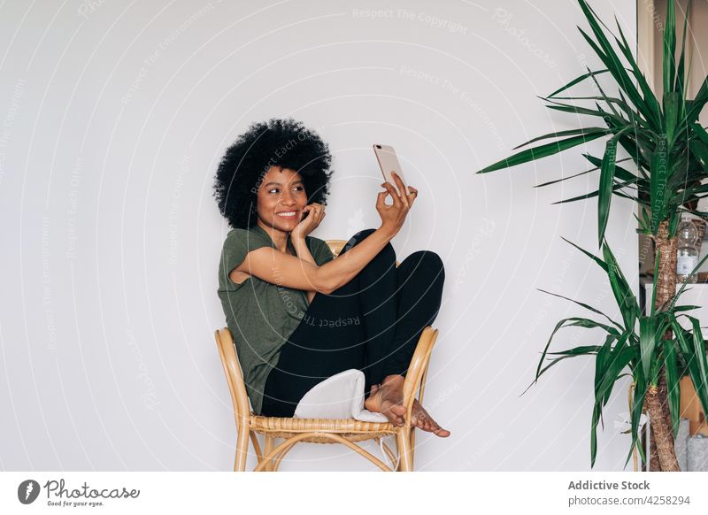Positive schwarze Frau macht Selfie in der Nähe von grünen Topfpflanzen positiv Lächeln Glück Pflanze eingetopft Smartphone fotografieren heiter benutzend