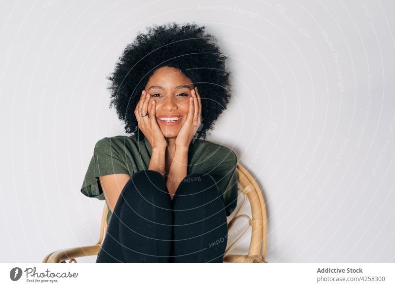 Glückliche schwarze Frau, die ihr Kinn auf die Hände auf einem Holzstuhl stützt Vorschein froh Lächeln positiv selbstbewusst Zeitgenosse charismatisch Freude