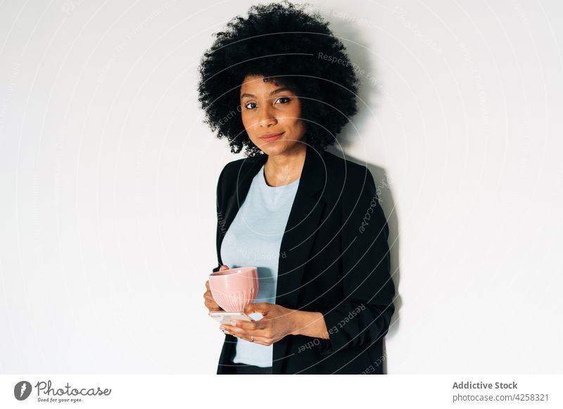 Positive schwarze Frau mit Tasse und Smartphone positiv Mobile Telefon elegant Anzug Optimist Individualität Becher Apparatur Vorschein formal Afroamerikaner