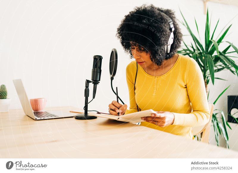 Junge schwarze Frau, die ein Notizbuch schreibt, während sie einen Podcast im Studio aufnimmt Notebook schreiben Aufzeichnen strömen Mikrofon Arbeit Radio