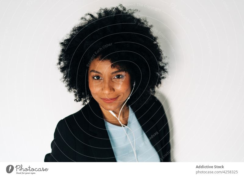 Positive schwarze Frau, die über Kopfhörer Musik hört positiv Lächeln heiter elegant Anzug Smartphone zuhören Glück froh Afroamerikaner benutzend Optimist