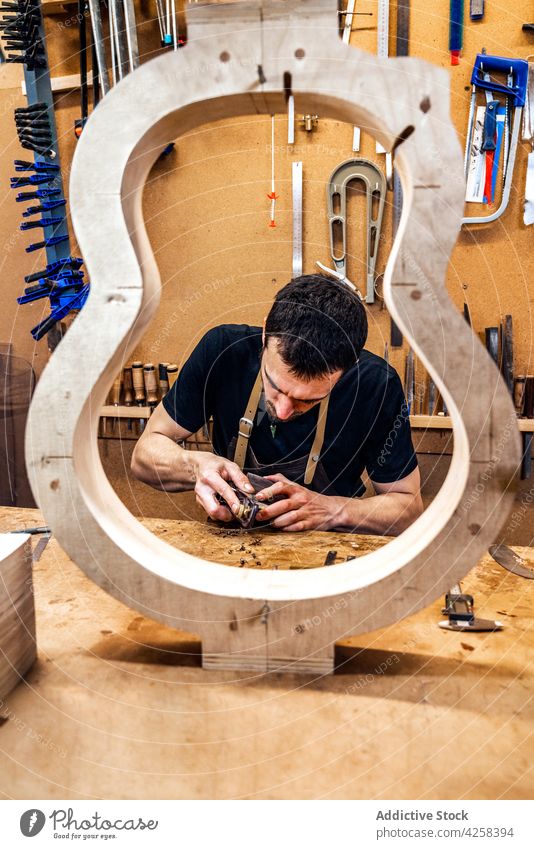 Konzentrierter Handwerker, der beim Gitarrenbau mit Holz arbeitet Kunstgewerbler verflachen Holzarbeiten Ebene machen Instrument achtsam Mann Kleinunternehmen