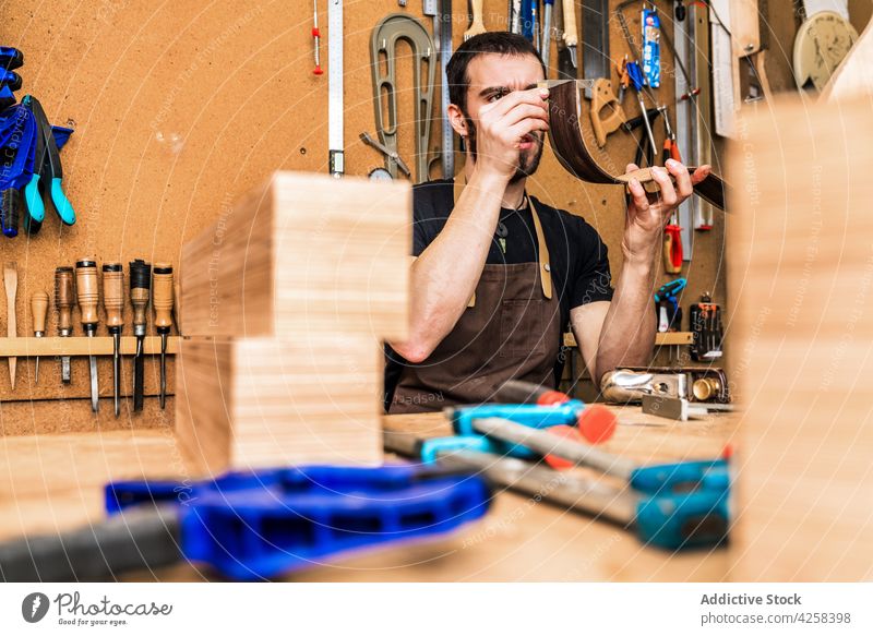 Kunsthandwerker bei der Kontrolle eines Holzstücks im Werkraum Kunstgewerbler prüfen Holzarbeiten Spielfigur präzise Genauigkeit Mann Werkstatt Kleinunternehmen