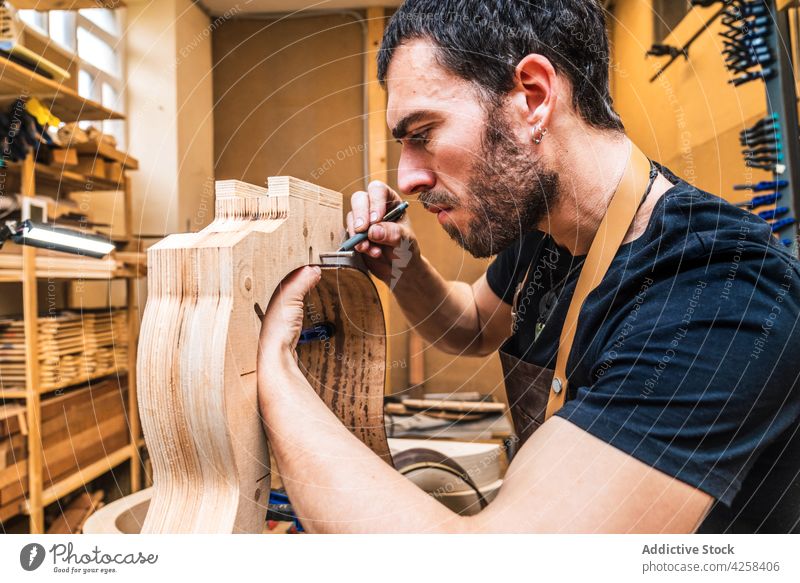 Ein Geigenbauer markiert ein Holzstück beim Bau einer Gitarre im Werkraum Kunstgewerbler Mark Holzarbeiten bauen präzise Genauigkeit Fokus Mann Kleinunternehmen