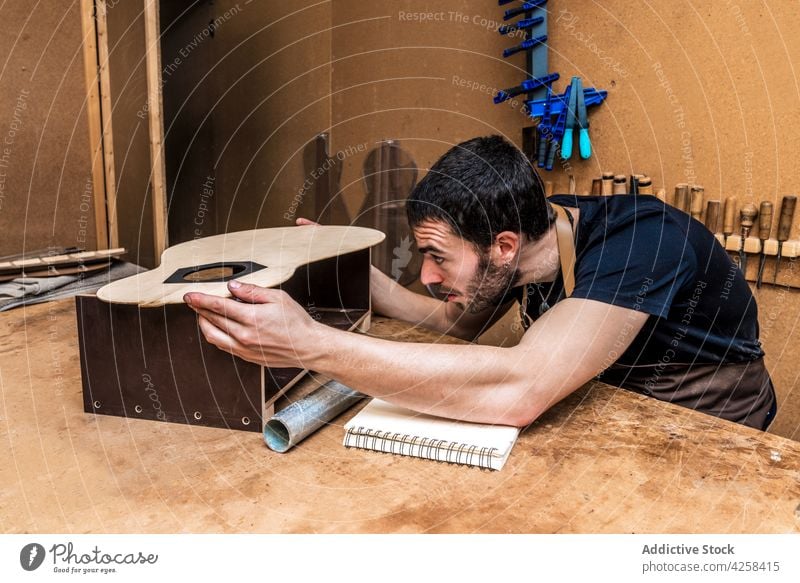 Handwerker prüft ein Gitarrenstück im Arbeitsraum Kunsthandwerker untersuchen Spielfigur Beruf Holzarbeiten präzise Fokus Werkstatt Kleinunternehmen Mann